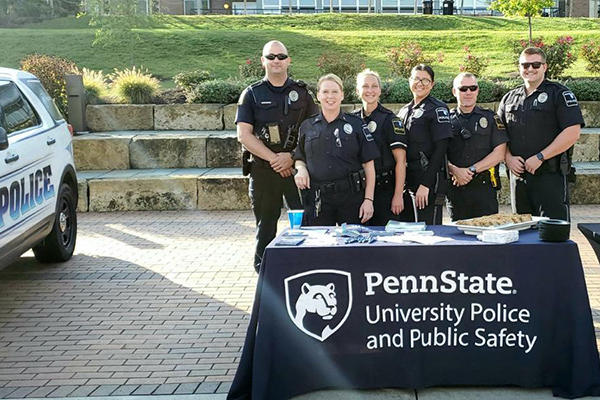 A group of police offfers posing behind a table beside a police vehicle.