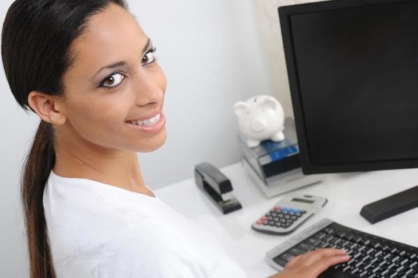 Person smiling at the camera as they work at a computer.